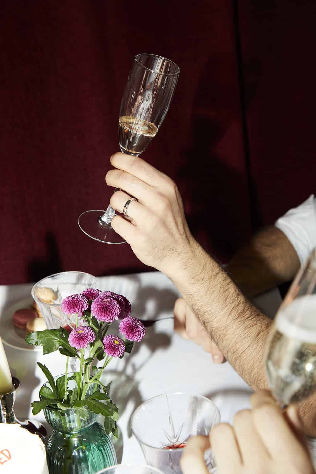 Een persoon met een glas champagne staat op een tafel met bloemen en drankjes.