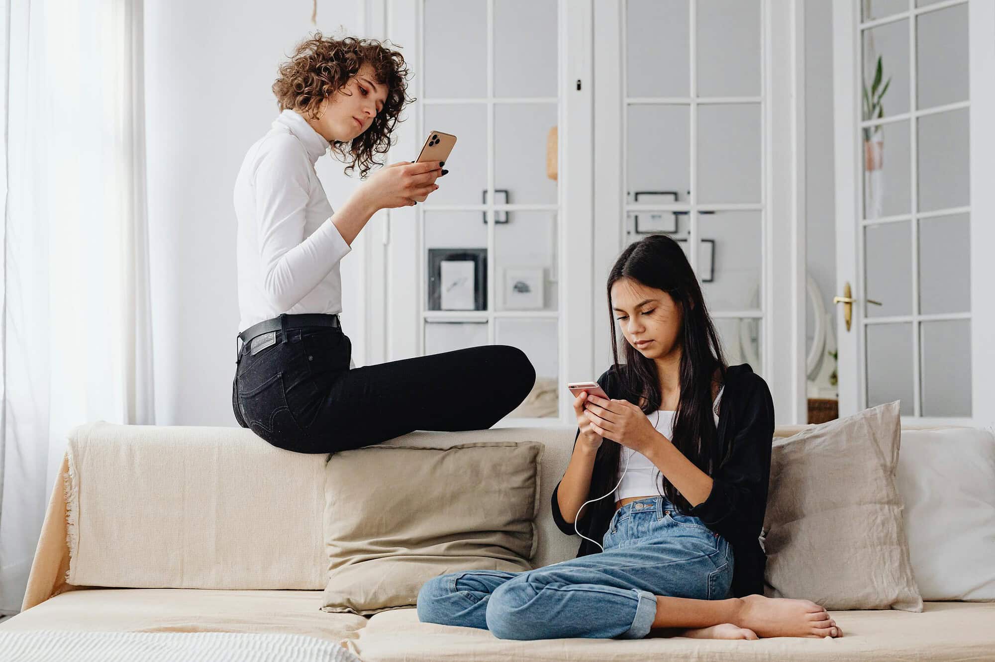 Two women using smartphones while seated on a couch in a modern living room setting.
