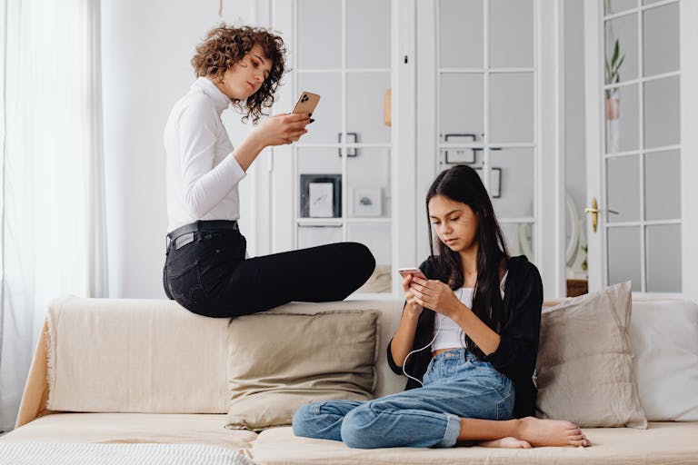 Two women using smartphones while seated on a couch in a modern living room setting.